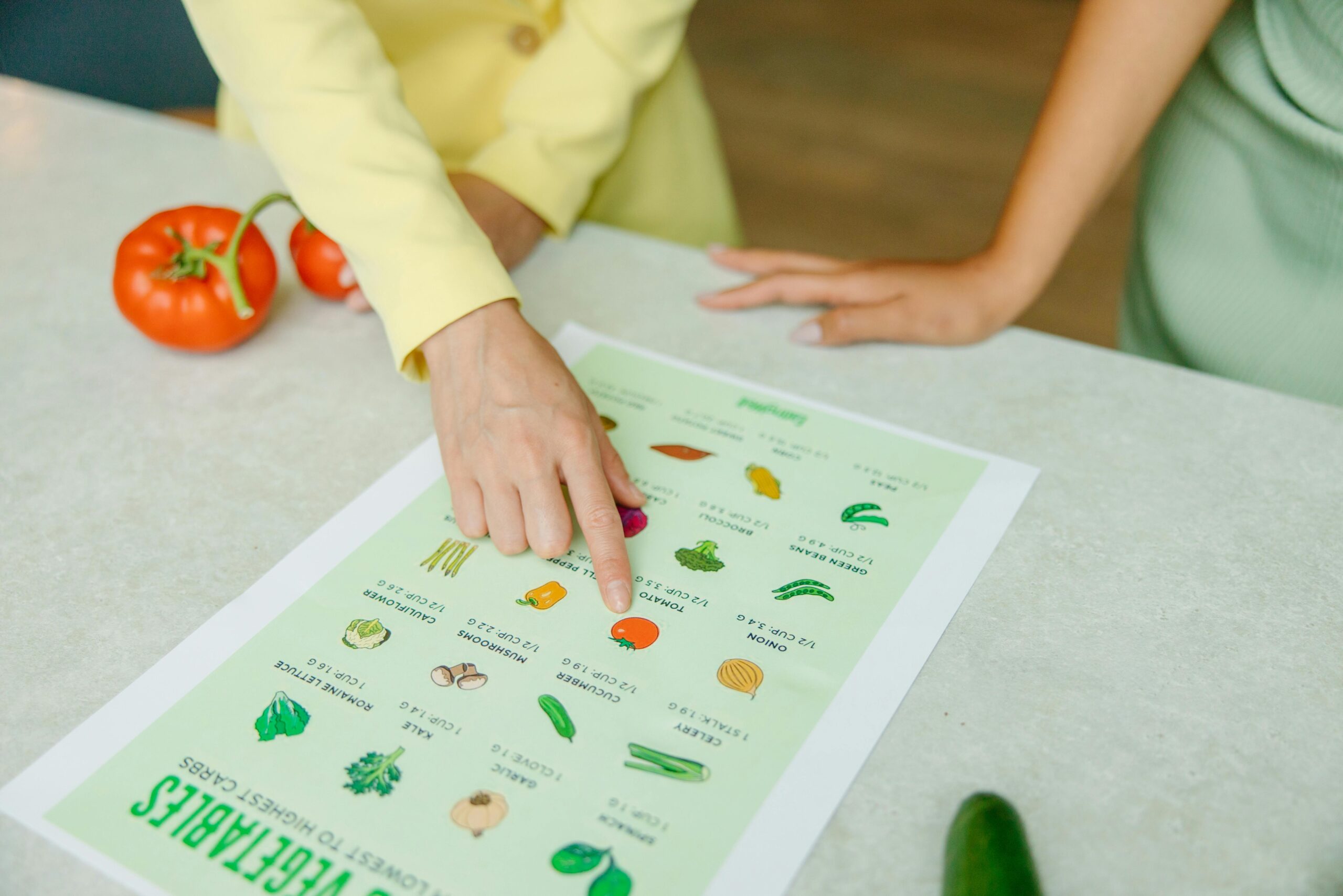 Visual recipes, Close-up of hands pointing to a vegetable nutrition chart with fresh tomatoes on the table.