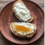 wo slices of toasted bread on a brown plate, topped with cream cheese and sprinkled with cinnamon powder, a simple fall harvest toast recipe for toddlers.