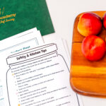 Cooking safety tips on a paper beside a green folder and three peaches on a wooden board. Bright, organized, and educational kitchen setting.