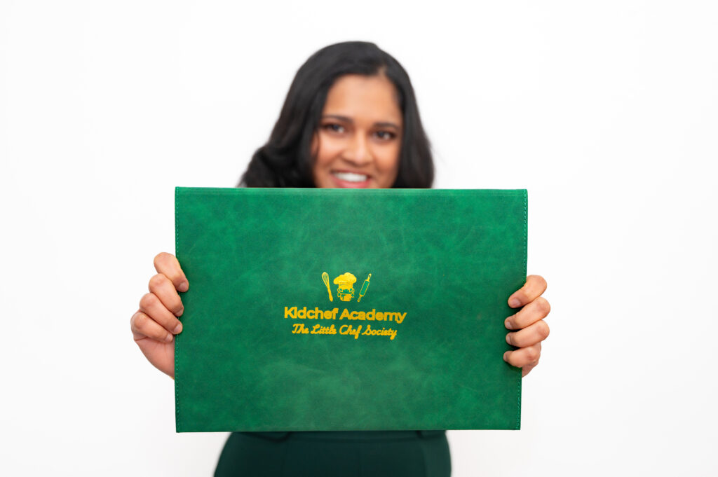 Founder smiling, showing the green Kidchef Academy Playbook master folder